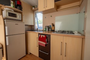 A compact kitchen with a microwave, refrigerator, stove, and wooden cabinets.