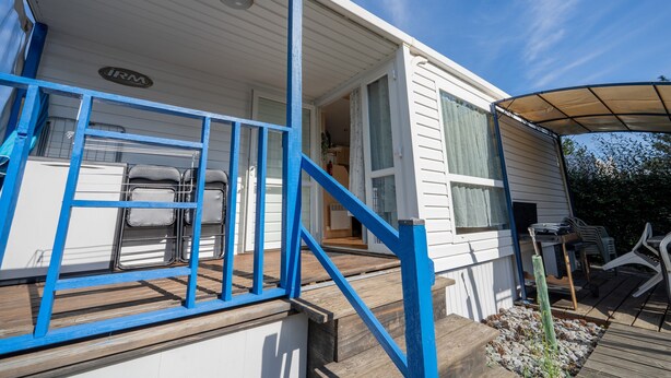 Une maison mobile dotée d’une véranda, d’un escalier et d’un petit jardin.