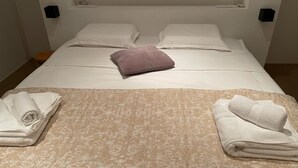 Een net opgemaakt bed met witte lakens, een gebreid plaid en opgerolde handdoeken aan beide kanten.