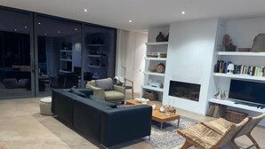 Een moderne woonkamer met een donkere bank, een houten salontafel en rieten stoelen.