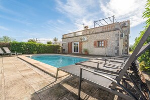 Un bâtiment en pierre doté d’une piscine, de chaises longues et d’une petite table.