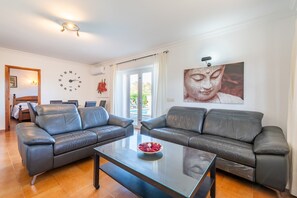 Un salon avec deux canapés en cuir, une table basse en verre, une horloge murale et une statue de Bouddha.
