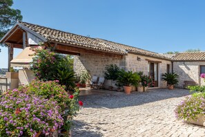 Un bâtiment en pierre avec un toit en tuiles, un patio couvert et des plantes en pot.