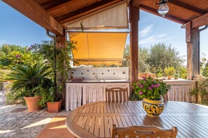 Une terrasse extérieure avec une table en bois, des chaises, une plante en pot et un mur recouvert de carreaux.