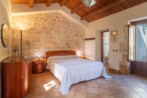 A bedroom with a stone wall, wooden ceiling, a bed, bedside tables, and a mirror. - Apartment 'Il Flauto Magico' with Private Terrace, Wi-Fi and Air Conditioning (Modica)