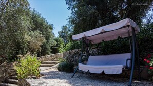 Un jardí amb mur de pedra, cadira penjant i una pèrgola.