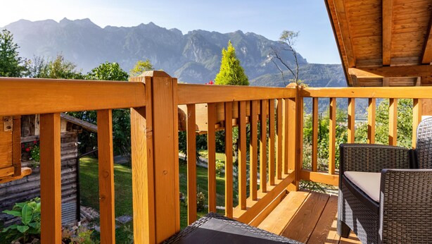 A wooden deck with wicker furniture, a view of mountains, and a wooden cabin in the background. - Chalet 'Maso Gigi' with Mountain View, Private Garden and Wi-Fi (Ivano fracena)