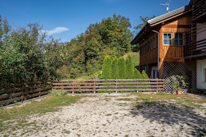 A wooden building with a fenced yard, a gravel path, and dense trees in the background.