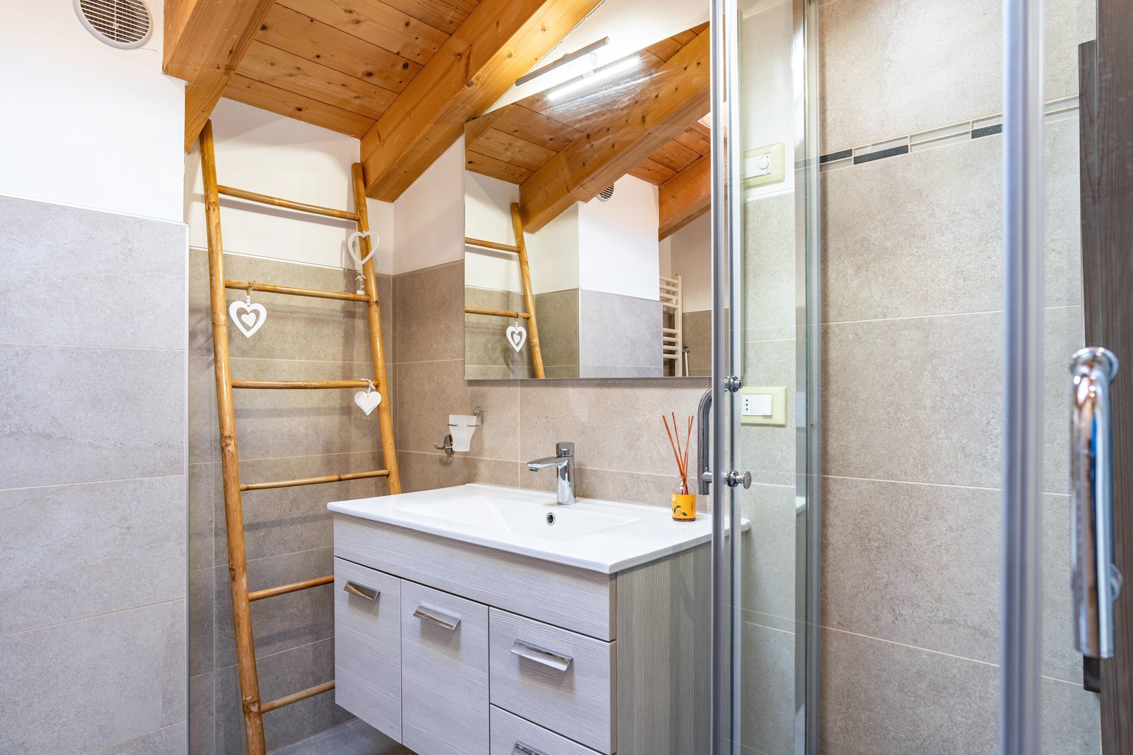 Un baño con una escalera de madera, un lavabo blanco y una cabina de ducha de vidrio.