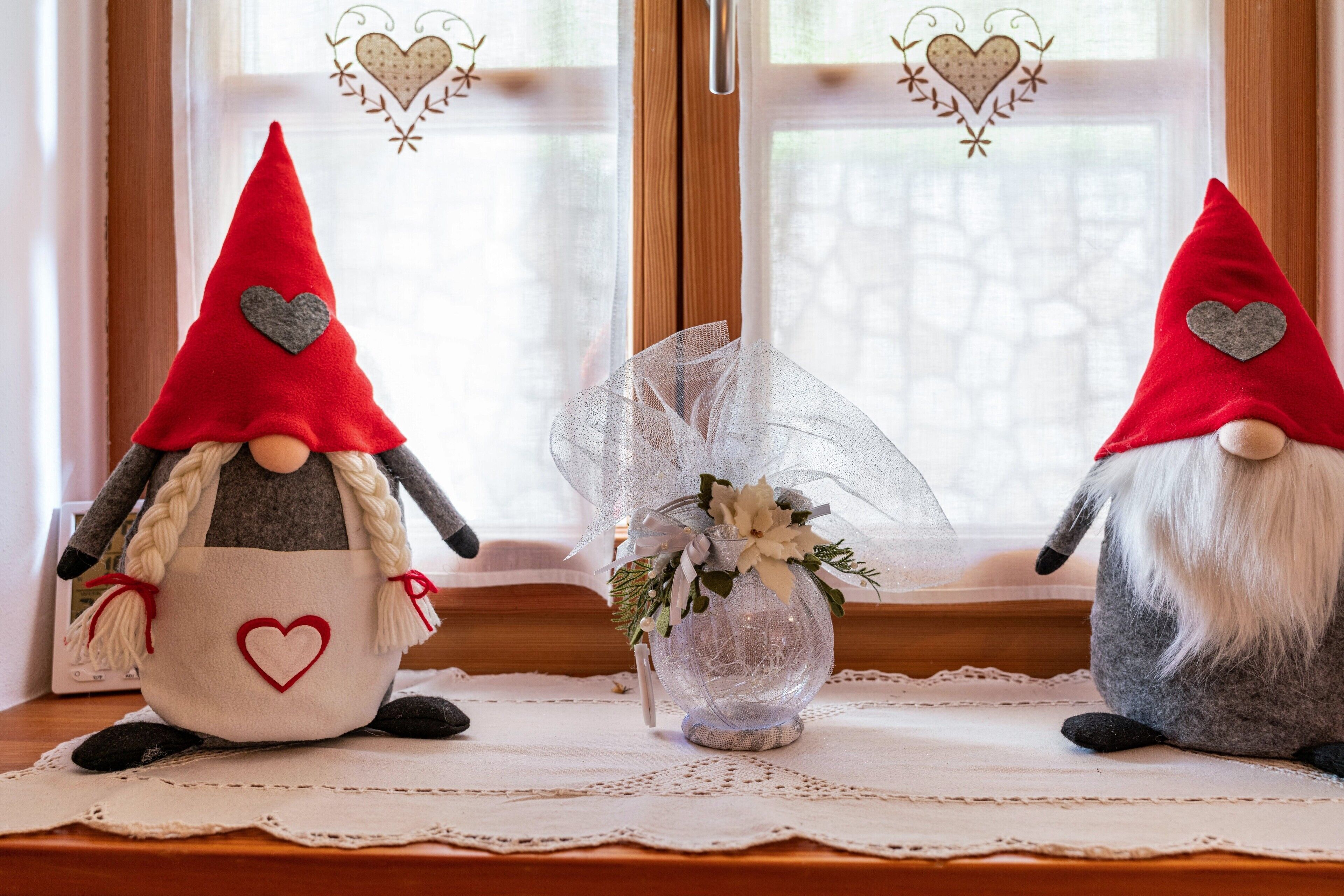 Two decorative gnome figures with heart motifs on a table near a window with heart-shaped decorations.