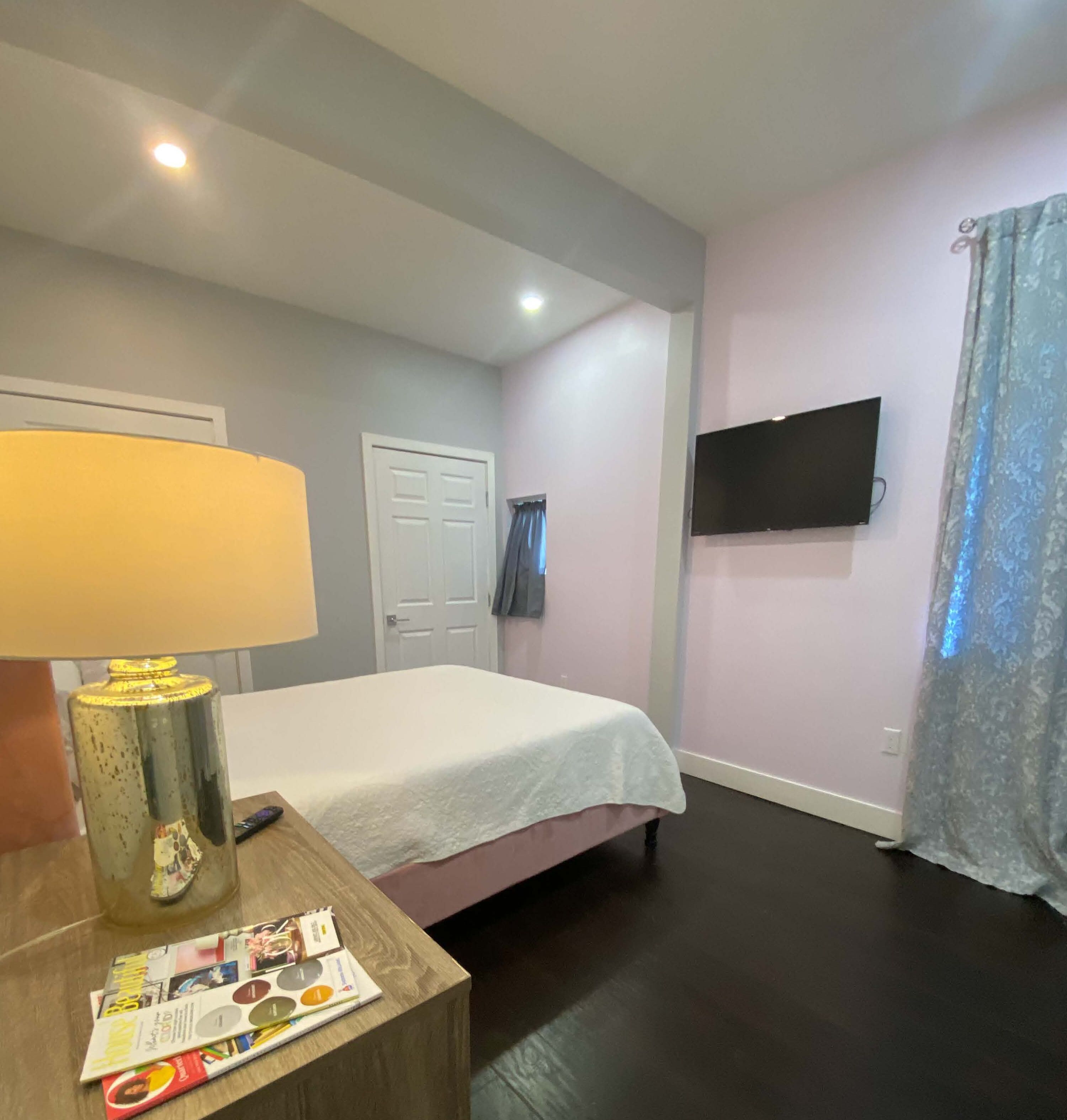 Une chambre à coucher avec un lit, une table de chevet avec une lampe, un téléviseur fixé au mur et une porte.