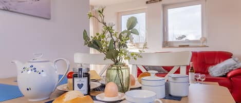 A dining table with a teapot, cups, plates, and a vase with flowers.