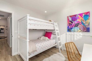 A bunk bed with a ladder, a white chair, and a colorful abstract painting on the wall.