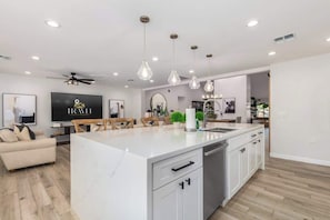 A modern kitchen with a central island, pendant lighting, and a dining area with a sofa and chairs.