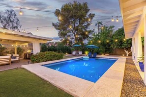 A swimming pool with a patio area, string lights, and outdoor furniture.