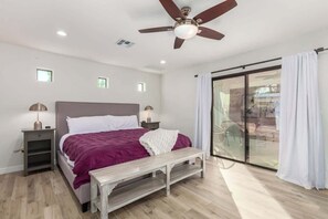 Un dormitorio con cama, mesitas de noche, ventilador de techo y puerta corrediza de vidrio al exterior.