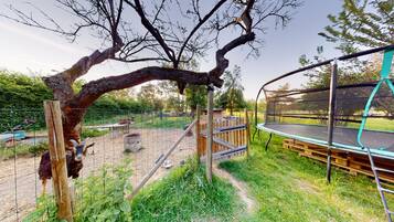 Un espacio exterior cercado con un banco de madera, un trampolín y una zona de alimentación.