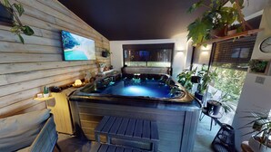 A hot tub area with wooden walls, a mounted TV, and potted plants. - Le Souffle du Saule (Buhl-Lorraine)
