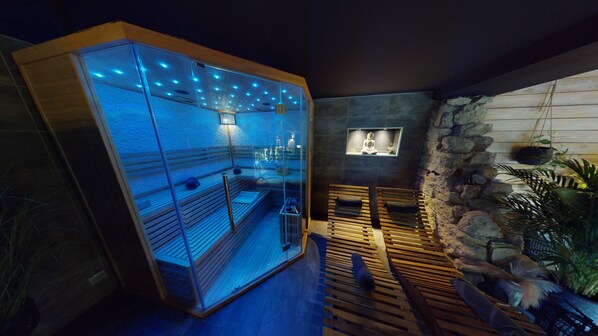 Een wellnessruimte met een sauna met glazen wand, houten banken en een stenen muur met een Boeddhabeeld.