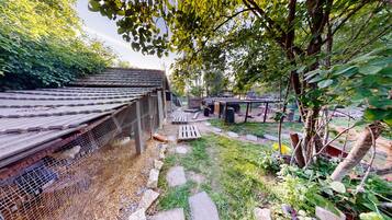 A rustic outdoor area with a wooden structure, a fenced enclosure, and a pathway leading to a covered seating area.