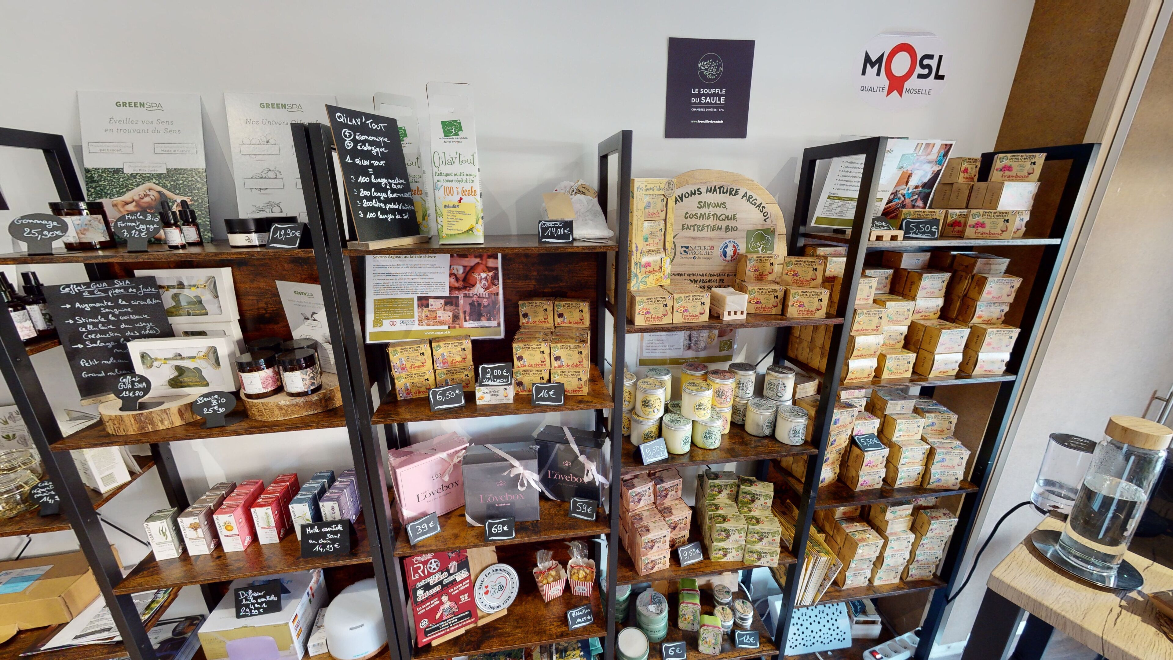 Una tienda con estantes repletos de diversos productos, como frascos, cajas y botellas. Se observan letreros con precios y nombres de los productos.