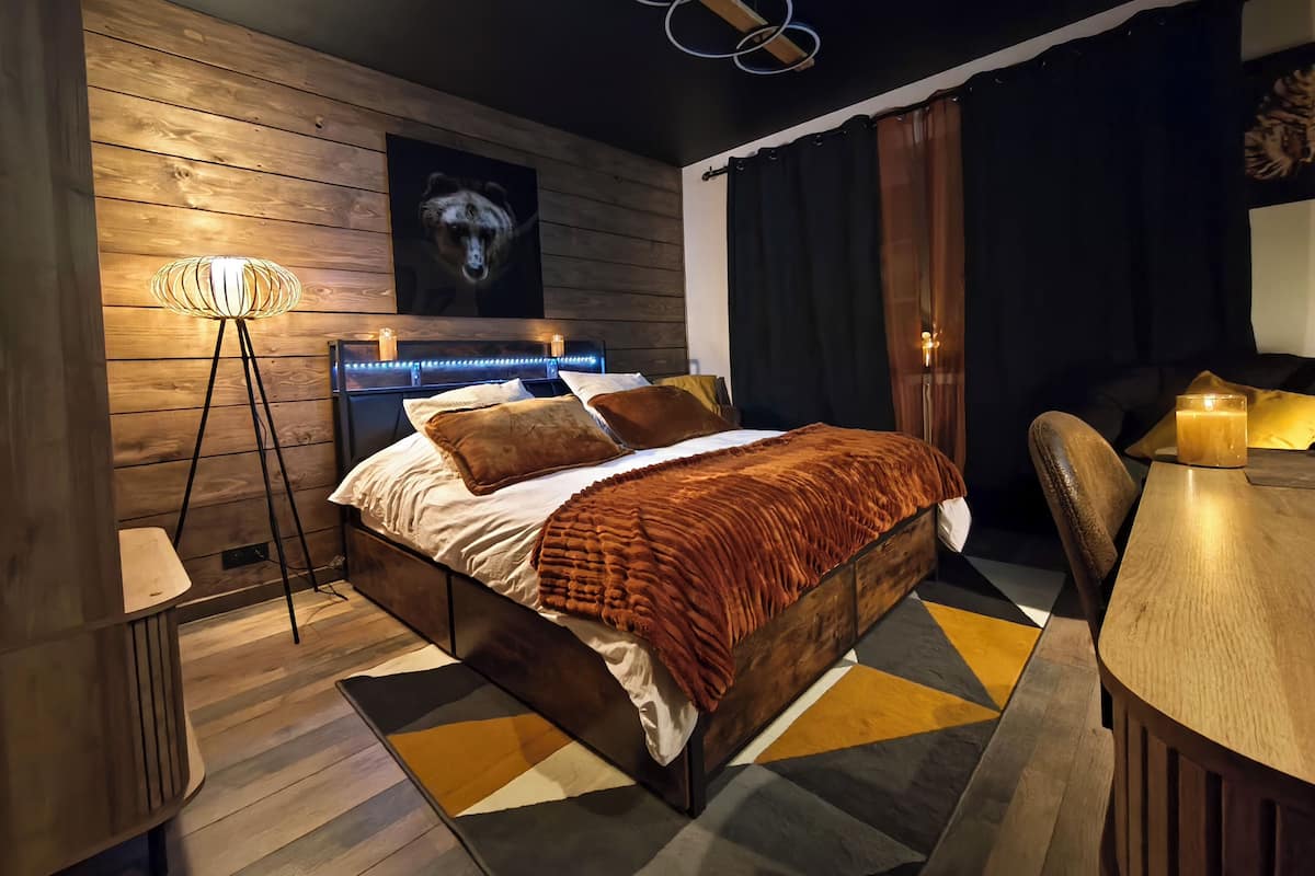 Een moderne slaapkamer met een houten hoofdbord, een vloerlamp, een nachtkastje en een vloerkleed met een geometrisch patroon.