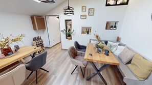 Een moderne woonkamer met een houten eettafel, twee banken en een salontafel. Er staan decoratieve objecten, zoals een vaas met bloemen en een wandplank met flessen.