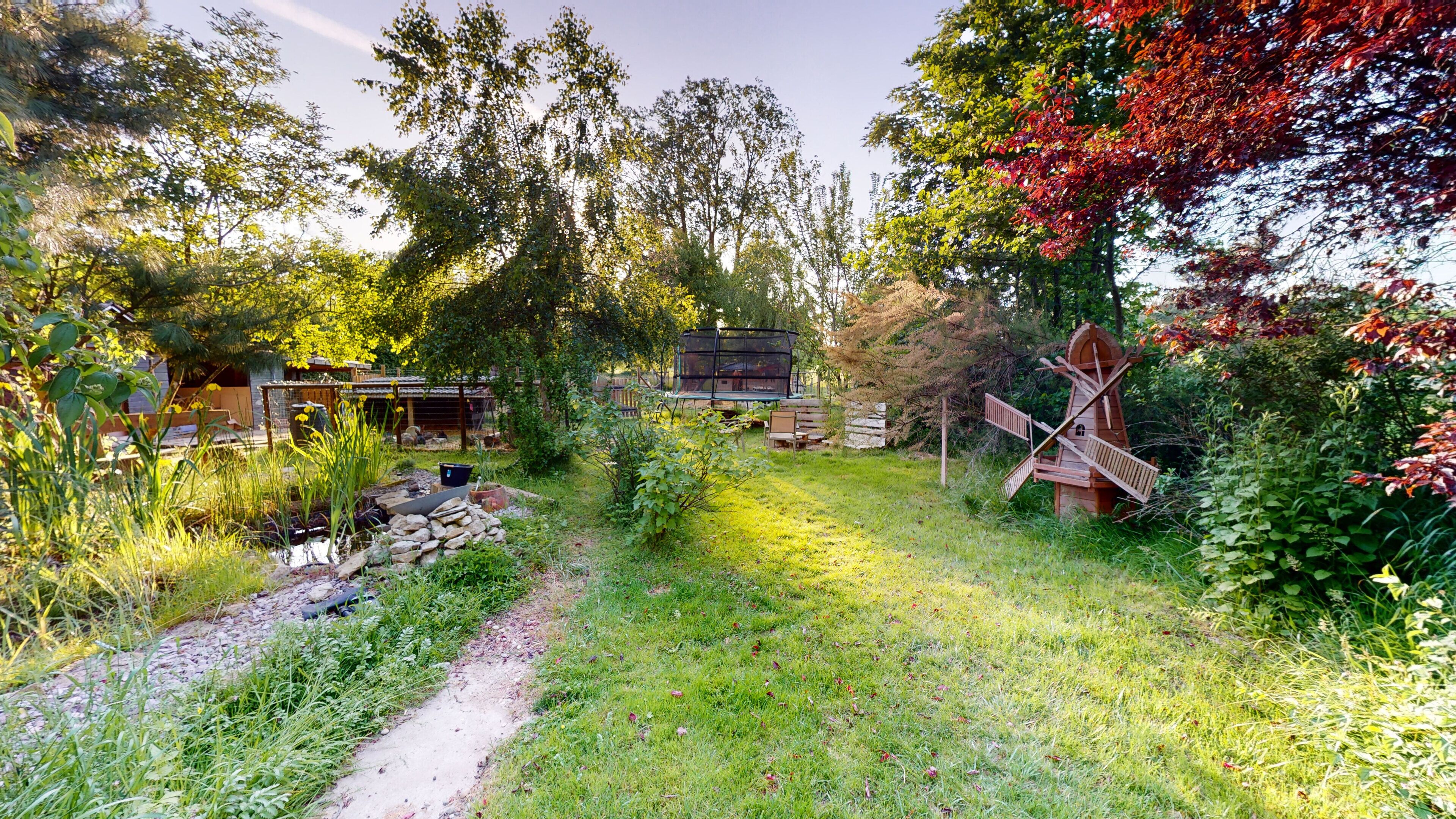 A garden with a wooden windmill, a wooden structure, and a stone wall.