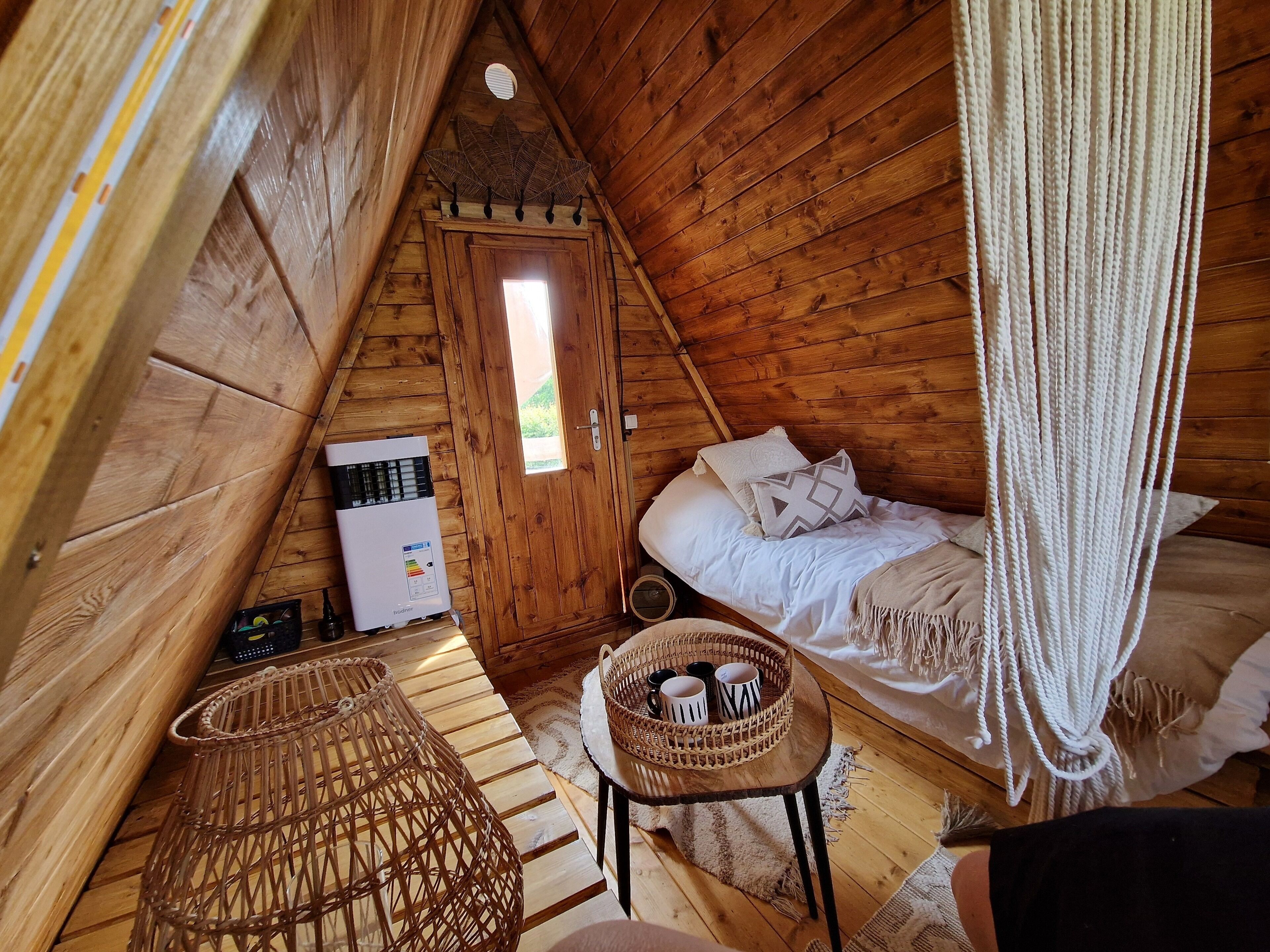 A cozy attic bedroom with a bed, a small table with mugs, a wicker chair, and a ceiling fan.