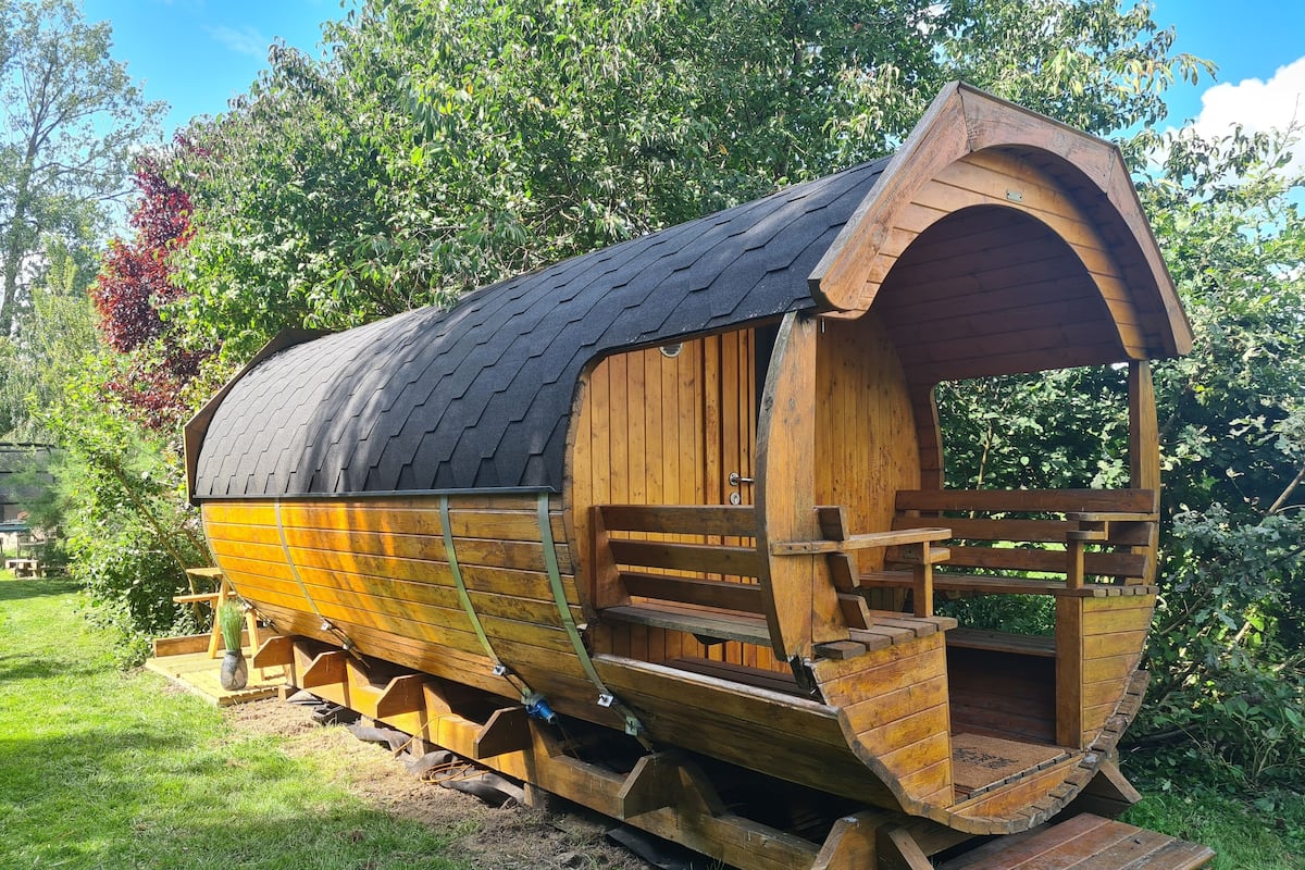 Een houten constructie in de stijl van een trekkerswagen, met een gebogen dak, houten trappen naar een ingang en een klein terras.