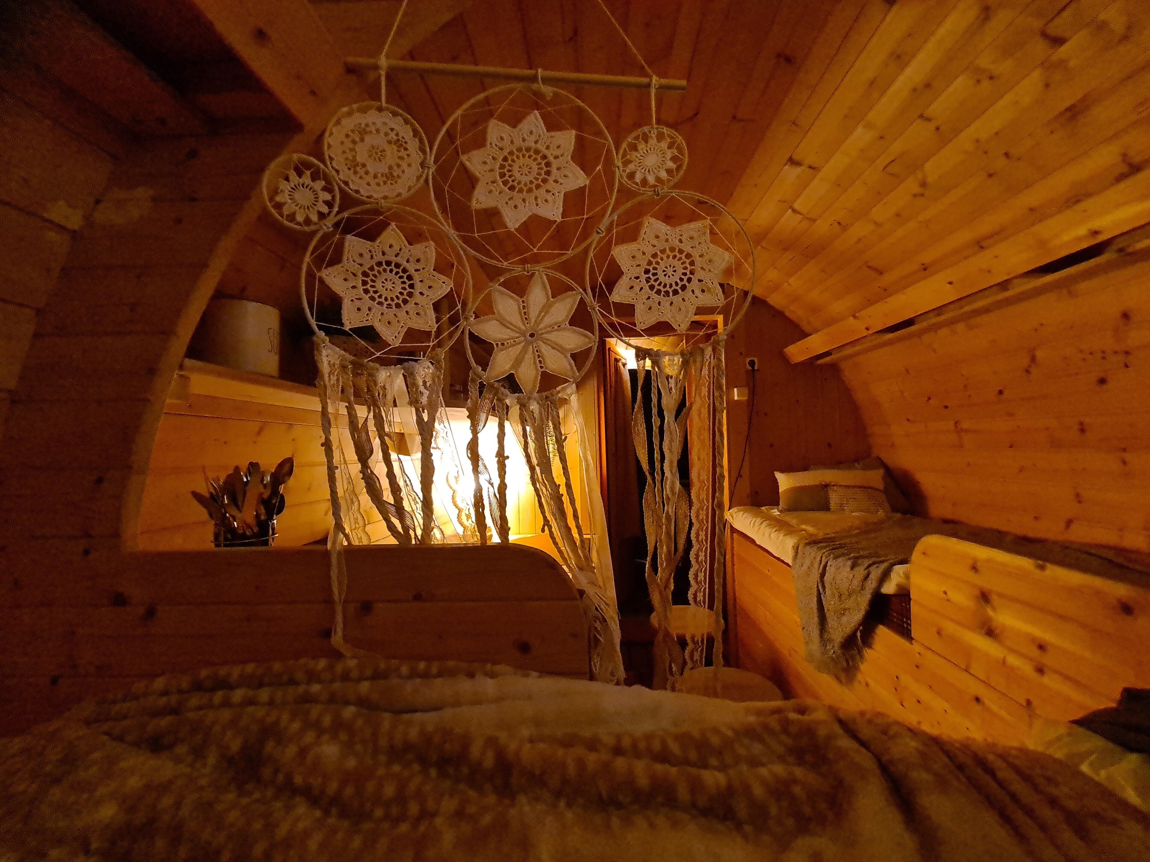 A cozy attic bedroom with a sloped ceiling, wooden walls, a bed with a white blanket, and a window with curtains.