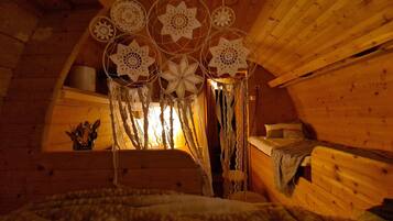 A cozy attic bedroom with a sloped ceiling, wooden walls, a bed with a white blanket, and a window with curtains.