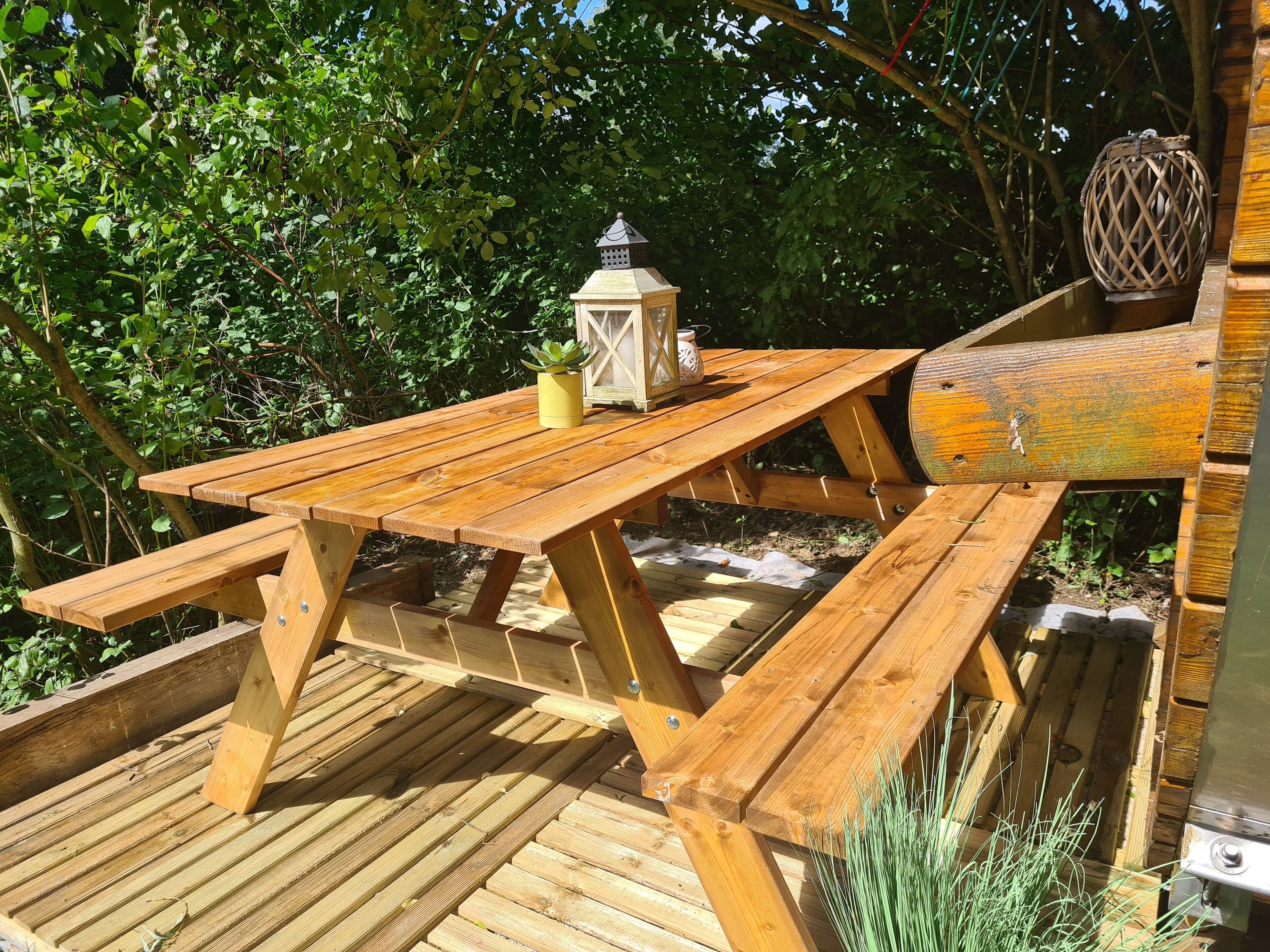 Een houten picknicktafel met bankjes, omringd door groen en een lantaarn.