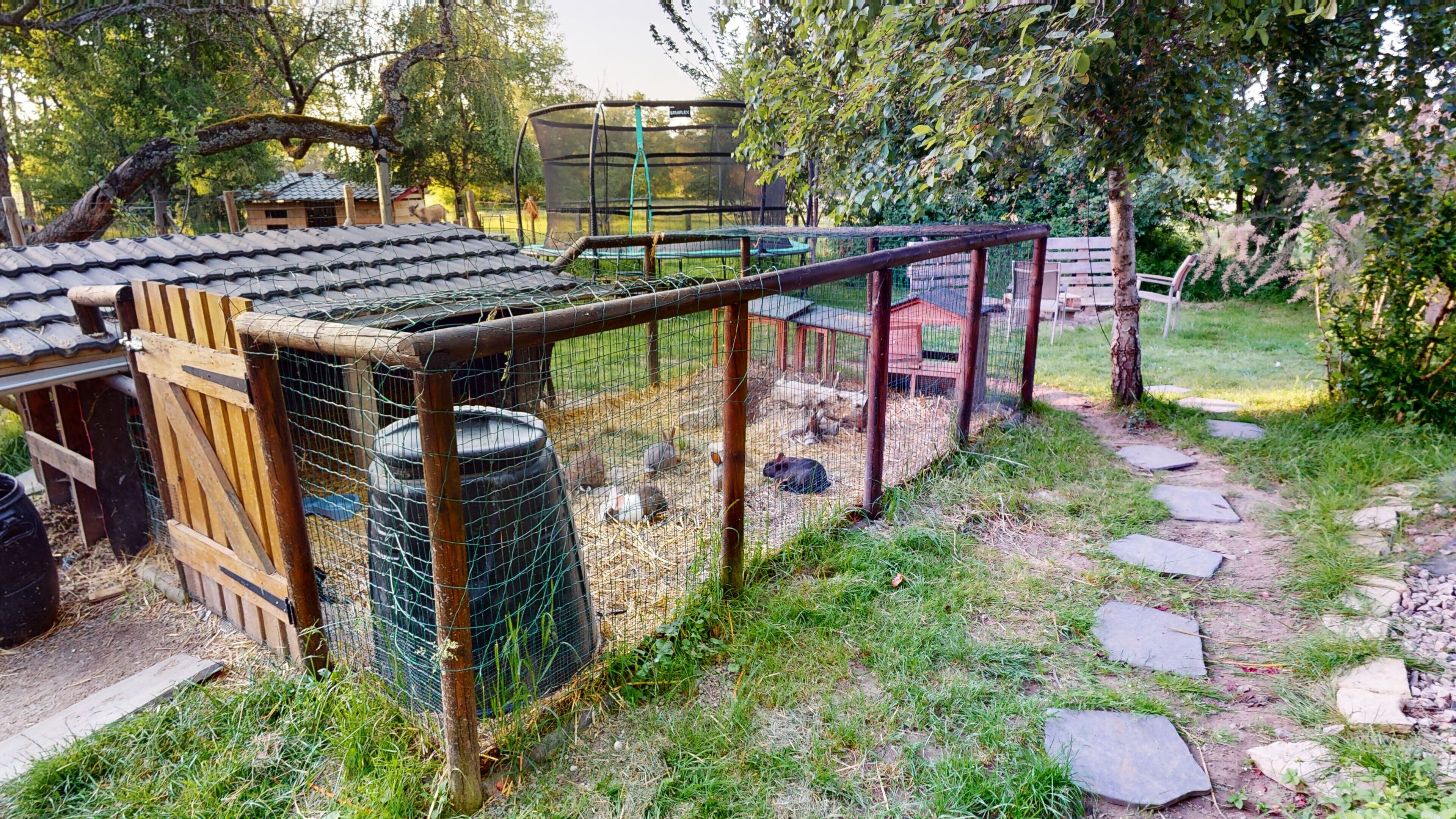 A fenced outdoor area with a wooden structure, a metal barrel, and a stone path.