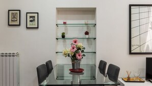 Ein moderner Essbereich mit einem Glastisch, schwarzen Stühlen, einer Blumenvase und einer Glasablage mit Dekoration.