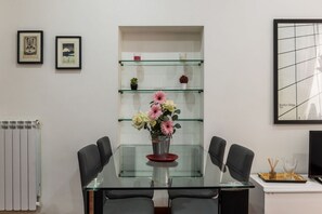 A modern dining area with a glass table, black chairs, a vase of flowers, and a glass shelf with decorative items.