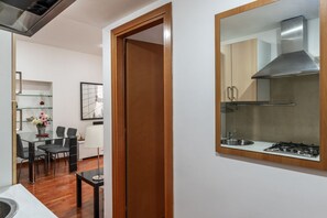 Una cuina moderna amb una campana d'extracció d'acer inoxidable, un rentaplat i una placa de cocció. Hi ha una zona de menjador amb una taula de vidre i cadires.