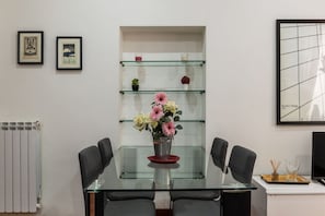 A modern dining area with a glass table, black chairs, a vase of flowers, and a glass shelf with decorative items. - A pochi passi da Fontana di Trevi (Roma)