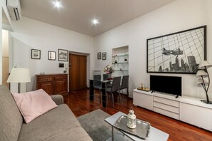 A modern living room with a sofa, a dining table with chairs, a TV, and a painting on the wall. - A pochi passi da Fontana di Trevi (Roma)