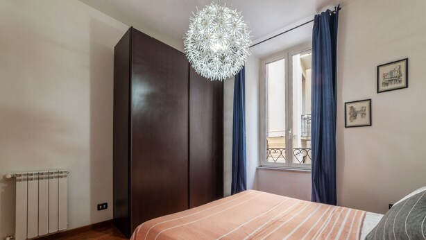 Une chambre à coucher comprenant un lit, une armoire, un radiateur, une fenêtre avec des rideaux et un lustre.