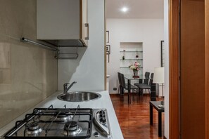 Cuina compacta amb fogó de gas, rentat i zona de dinar amb cadires i taula.