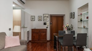Un salon comprenant un canapé, une table à manger avec des chaises, un meuble en bois et une étagère en verre ornée d’objets décoratifs.
