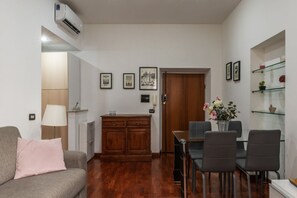Un saló amb un sofà, una taula de dinar amb caires, un armari de fusta i una prestatgeria de vidre amb objectes decoratius.