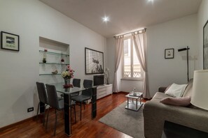 A modern living room with a glass dining table, grey sofa, and a TV.