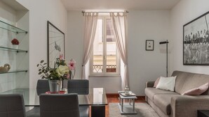 Ein modernes Wohnzimmer mit einem Glastisch, grauem Sofa und einem großen Fenster mit durchscheinenden Vorhängen.
