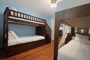 A bunk bed room with a wooden floor, a staircase, and a door leading to another room. - Spacious Home Prime Location Near Train, JFK, Dining, Shop, Parking & Essentials (Bellmore)