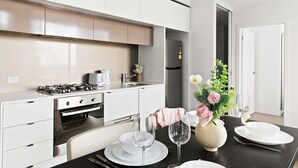 A modern kitchen with white cabinets, a gas stove, and a dining area with a table set for two. - Modern 2BR Apt Next to Victoria Market, City Views (Melbourne)