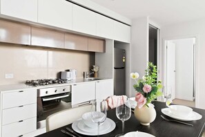 A modern kitchen with white cabinets, a gas stove, and a dining area with a table set for two. - Modern 2BR Apt Next to Victoria Market, City Views (Melbourne)