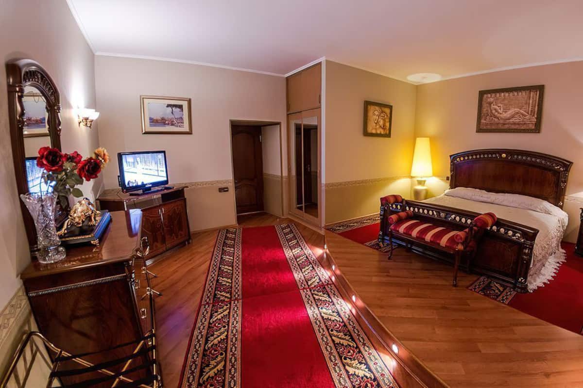Quarto de hotel com uma cama grande, uma escrivaninha com um computador, um espelho e um tapete vermelho.