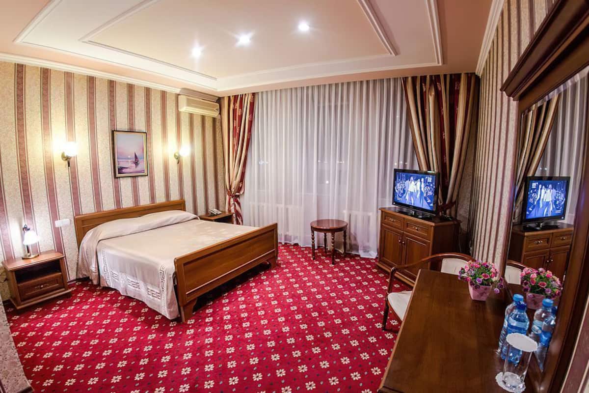 Quarto de hotel com cama, televisão, escrivaninha com cadeira e uma pequena mesa com flores e garrafas de água.